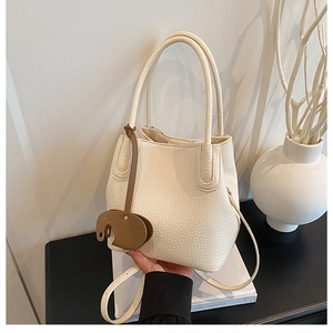 Détail du sac seau blanc crème avec motif litchi et un charm éléphant en cuir marron