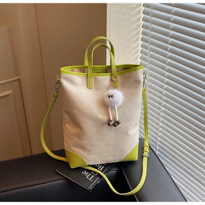 Detail of off-white canvas tote bag with vibrant green leather trim and cute plush charm