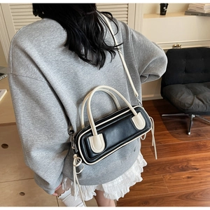 Dettaglio di una borsa a cilindro bicolore nero e crema con nodi decorativi in pelle