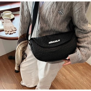 Close-up of black quilted saddle bag with wide strap in an autumn cafe setting