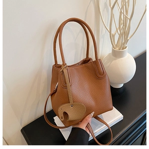 Détail d'un sac seau en cuir marron avec breloque éléphant posé sur des livres blancs