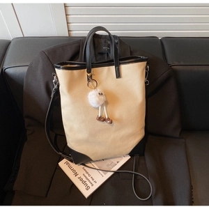 Detail of canvas tote bag with black leather trim and cute plush charm on a blazer
