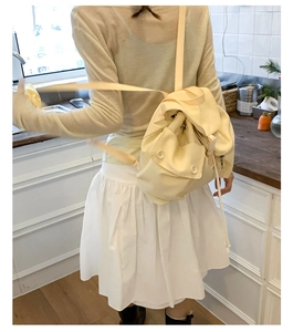 Close-up of cream nylon backpack with flap closure and vintage buttons shown on model