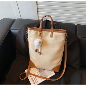 Close-up of canvas tote bag with leather trim and plush charm on black blazer