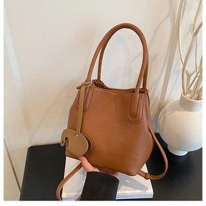 Détail d'un sac seau en cuir marron à motif litchi avec pendentif éléphant décoratif