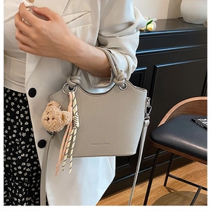 Detail of light gray lychee grain leather bucket bag with fashion logo and teddy charm
