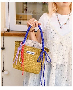 Detail of straw woven bucket bag with blue rope handles and On Our Own label