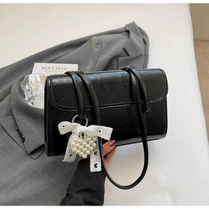 Detail of glossy black shoulder bag with lace bow and pearl heart charm accessory