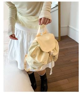 Close-up of a pale yellow canvas mini backpack with drawstring and flap buckle closure