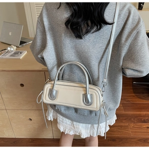 Detail of a minimalist cream crossbody bag with silver handles on a cozy indoor table