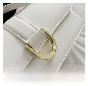Gros plan du sac carré en cuir blanc avec boucle fer à cheval dorée et surpiqûres
