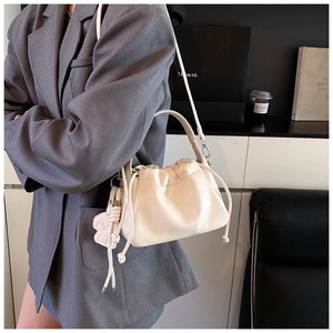 Detail of cream white pleated bucket bag with lychee texture and cute bear pendant