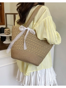 Straw tote beach bag with white lace bow detail shown in a stylish shoulder carry pose