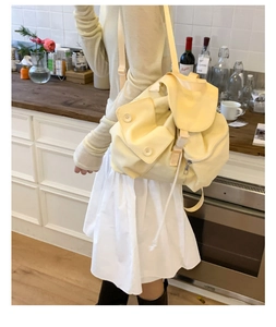 Detail of cream yellow nylon backpack with flap pocket and button in a cafe setting