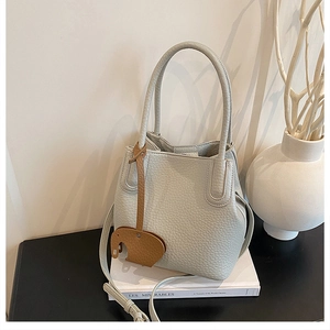 Détail du sac seau en cuir grainé avec breloque éléphant sur un livre blanc