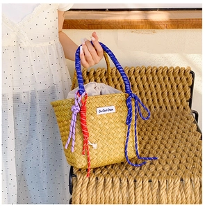 Detail of straw woven bucket bag featuring colorful rope handles and decorative knots