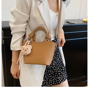 Close-up of tan leather bucket bag with decorative knot handle and plush bear charm