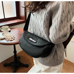 Close-up of black quilted saddle bag with letter logo and wide strap on model