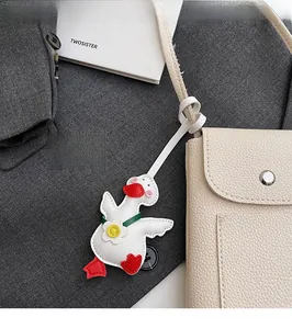 Detail of cute white leather goose charm with green tie attached to a beige bag strap