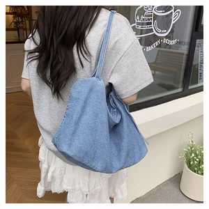 Outdoor shot of a blue denim tote bag with wide straps and washed texture detail
