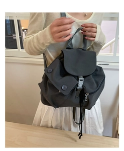 Detail view of dark grey nylon backpack featuring a drawstring closure and buckle flap