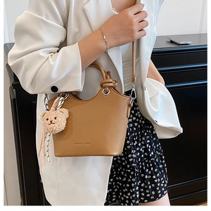 Brown textured leather bucket bag with knot handle and plush bear charm on model