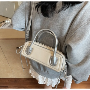 Detail showing beige baguette bag with silver handles and long fringe on a desk