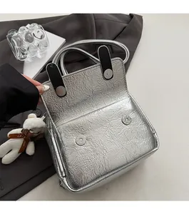 Detail view of silver pleated metallic tote bag with magnetic closure and small bear charm