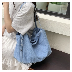 Detailed view of light blue denim tote bag with decorative silver eyelets on side