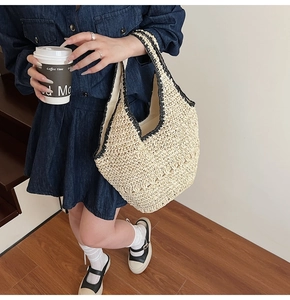 Detail of woven straw tote bag with black trim held by model in casual urban setting