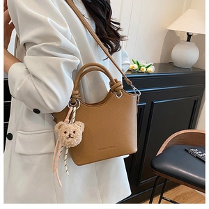 Brown lychee leather bucket bag detail with silver metal handles and a bear charm