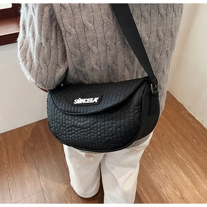 Detail of black quilted saddle bag showing vertical stitching and white letter logo