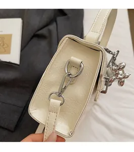 Detail of cream textured leather bag with silver hooks and balloon dog charm accessory