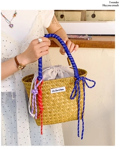Detail of hand-woven straw bucket bag with blue rope handle and decorative purple knots