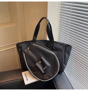 Detail of black faux leather badminton tote set with woven straps on a sofa