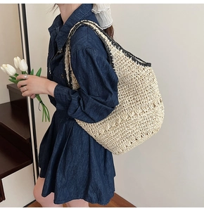 Detail of hollow woven straw shoulder bag featuring black braided trim for summer