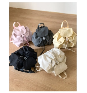 Flat lay of mini nylon backpacks in five colors including pink, yellow and black on wood floor