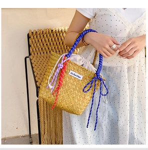 Detail of hand-woven straw bucket bag with vibrant blue rope handle and drawstring liner