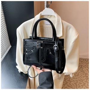 Détail d'un sac à main en cuir verni noir avec boucles décoratives et rivets métalliques