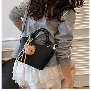 Close-up of black lychee leather handbag featuring a cute plush bear charm with ribbons