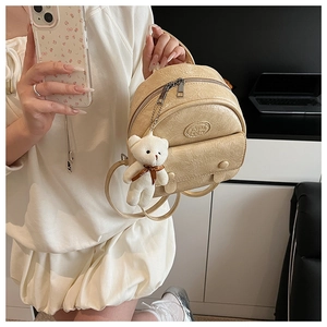 Close-up of beige mini backpack with wrinkled texture and cute white bear charm