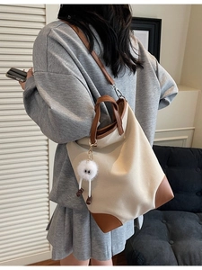 Large beige canvas tote bag with brown leather trim and plush charm worn by model