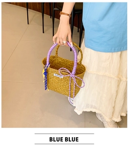 Detail of straw woven bucket bag featuring purple rope handle and decorative bow charm