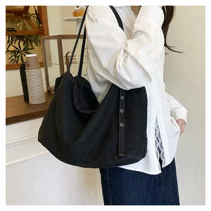 Detail of a large black canvas tote bag with metal eyelets and side straps on a model