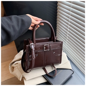 Détail d'un sac à main en cuir verni marron foncé avec boucles et rivets métalliques