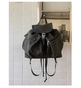 Detail view of dark grey canvas backpack showing flap buckle and drawstring closure texture