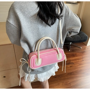 Detail view of pink leather barrel bag with cream handles and bow tassel on model
