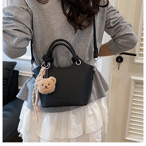 Detail of black pebbled leather bucket bag with cute plush bear and ribbon decoration