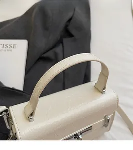 Close-up of off-white crocodile embossed texture with silver metal clasp and handle
