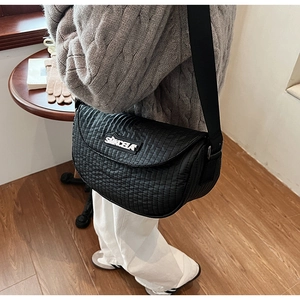 Detail of black quilted crossbody bag with vertical pleats and wide fabric shoulder strap